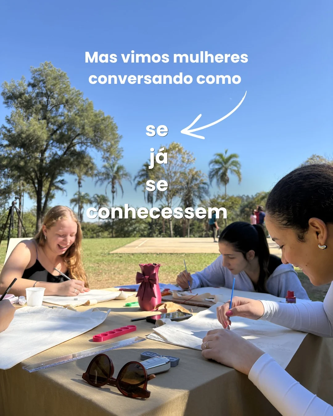 Participantes conversando junto à mesa de uma atividade de pintura em ecobag, com texto publicado pela Brava.